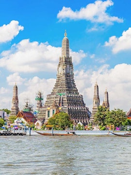 Wat Arun temple on Chao Phraya River, Bangkok, with boats in the foreground.