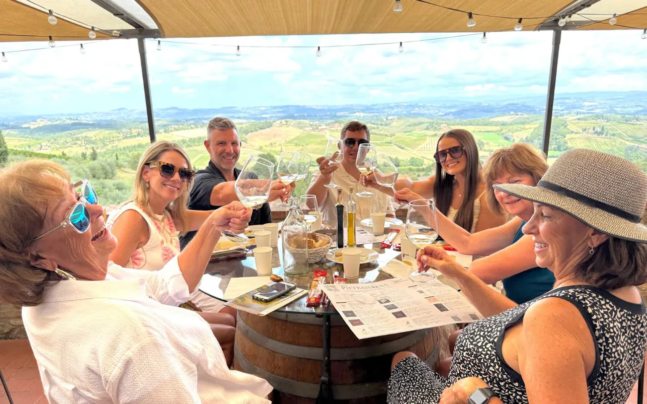 Group enjoying wine tasting at a Tuscan winery with scenic vineyard views.