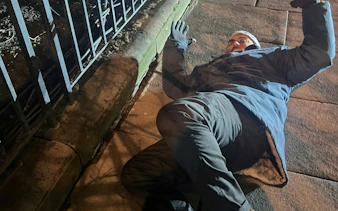 Man in winter clothing lying on a sidewalk during Edinburgh murder mystery game.