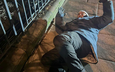 Man in winter clothing lying on a sidewalk during Edinburgh murder mystery game.