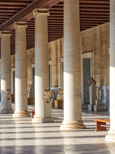 Ancient Agora of Athens colonnade with statues and sunlight streaming through columns.