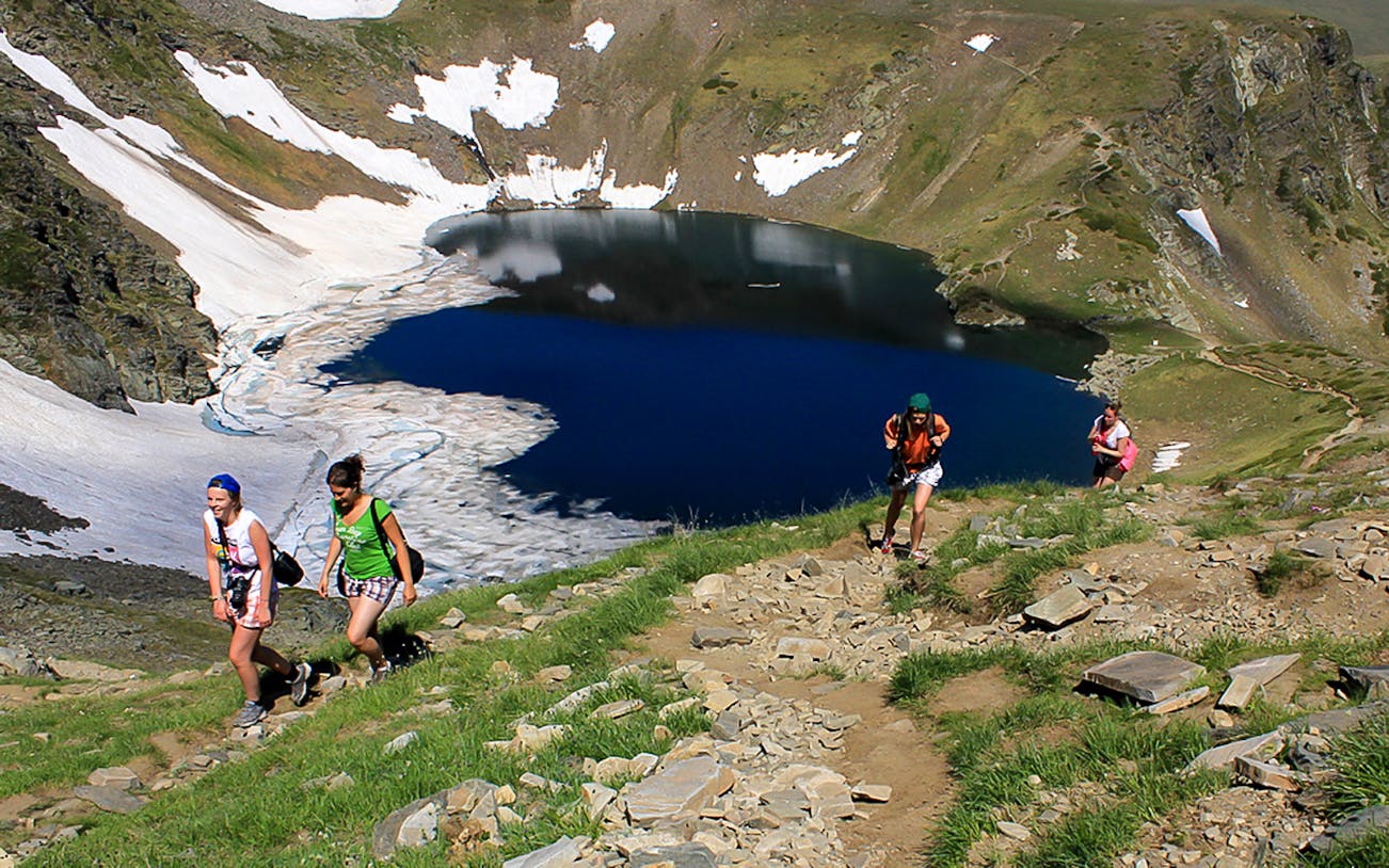 Guests hiking near Rila Lakes with snow patches and clear blue water in Bulgaria.