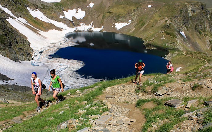 Guests hiking near Rila Lakes with snow patches and clear blue water in Bulgaria.