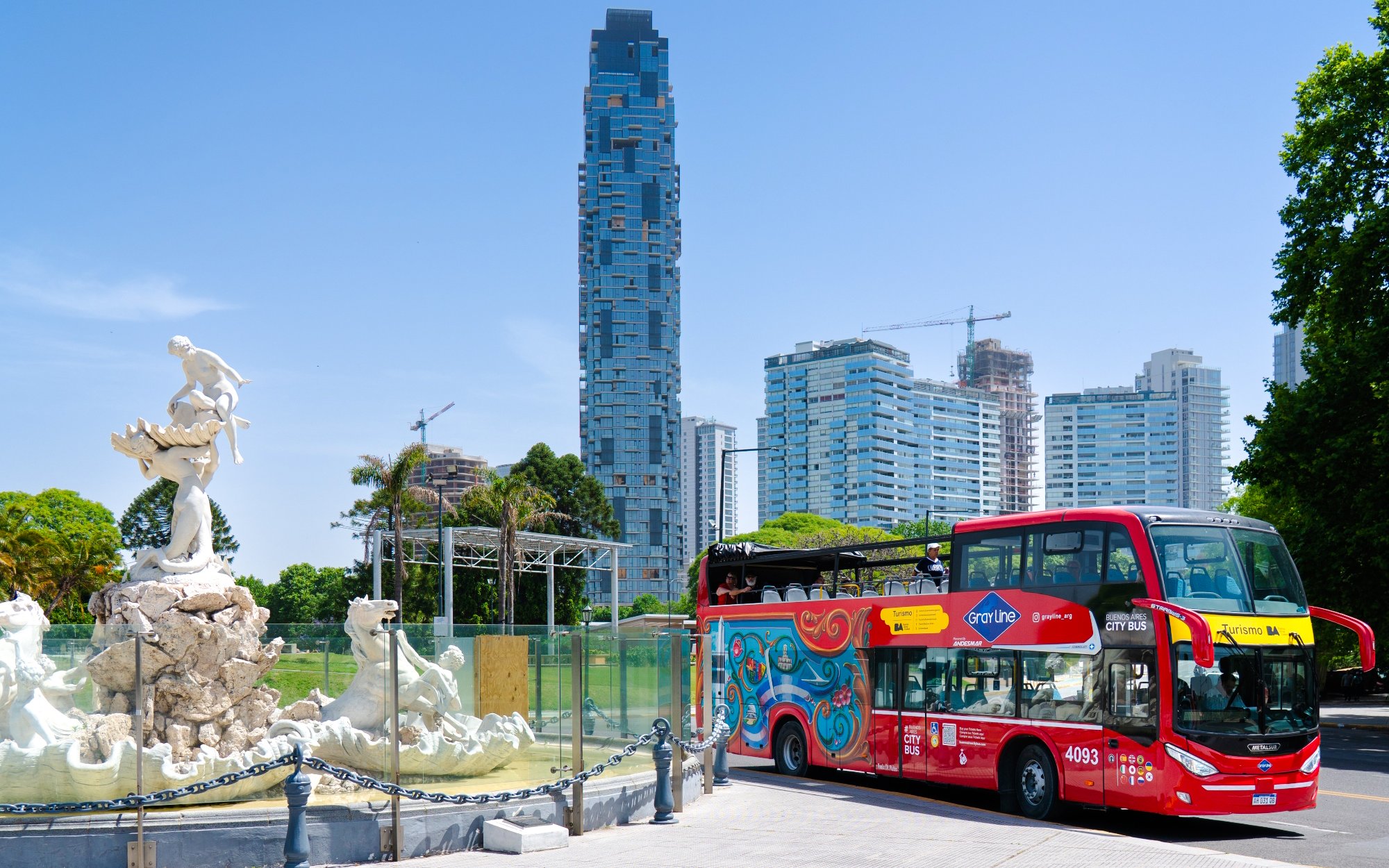 Hop-on Hop-off bus near Fuente de las Nereidas, Buenos Aires, with city skyline.