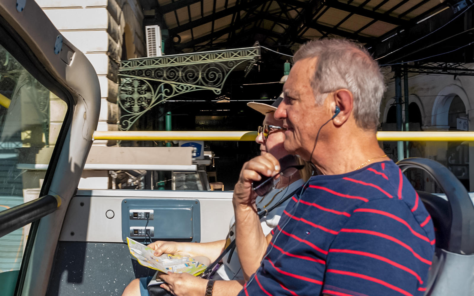 Passengers using audio guide on HOHO bus tour in Athens, Greece, with Acropolis in the background.