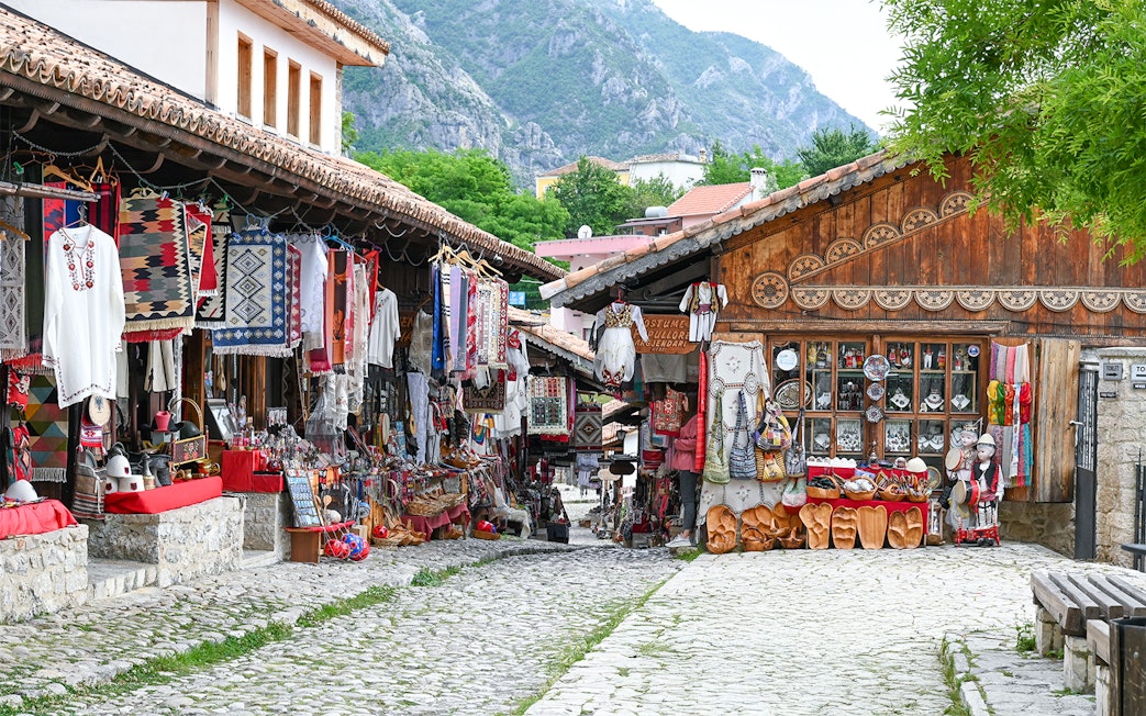 Old bazaar in Kruje, Albania with traditional textiles and crafts displayed along cobblestone street.