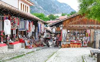 Old bazaar in Kruje, Albania with traditional textiles and crafts displayed along cobblestone street.