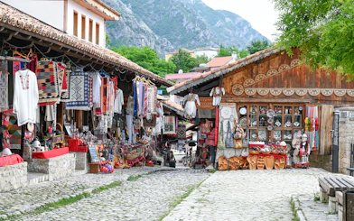 Old bazaar in Kruje, Albania with traditional textiles and crafts displayed along cobblestone street.