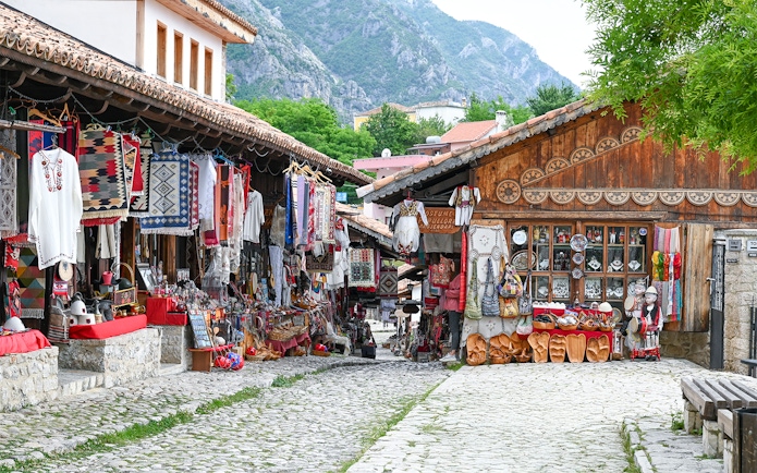 Old bazaar in Kruje, Albania with traditional textiles and crafts displayed along cobblestone street.