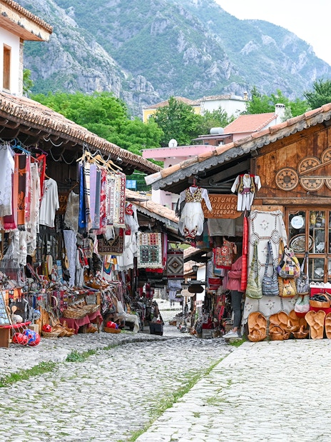 Old bazaar in Kruje, Albania with traditional textiles and crafts displayed along cobblestone street.
