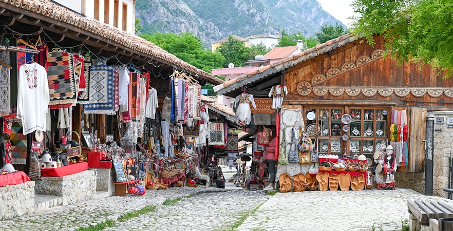 Old bazaar in Kruje, Albania with traditional textiles and crafts displayed along cobblestone street.