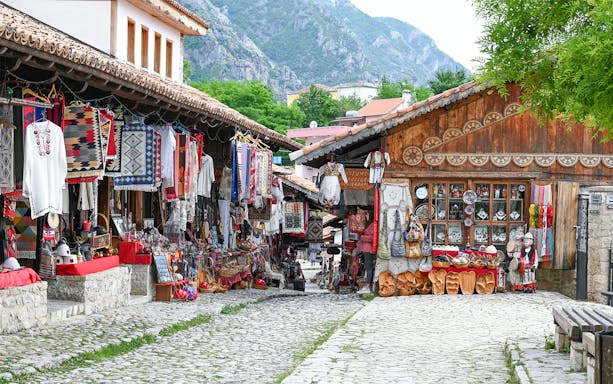 Old bazaar in Kruje, Albania with traditional textiles and crafts displayed along cobblestone street.