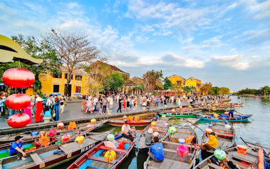 Boats with lanterns on the river in Hoi An, Vietnam, with people walking along the waterfront.