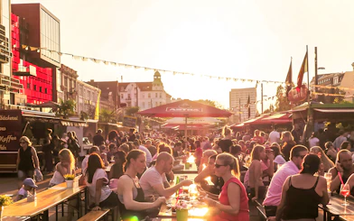 Outdoor dining scene at sunset in Hamburg with people enjoying food and drinks under umbrellas.