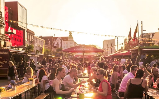 Outdoor dining scene at sunset in Hamburg with people enjoying food and drinks under umbrellas.