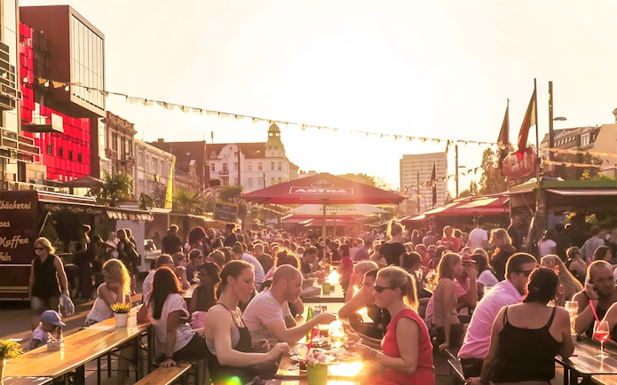 Outdoor dining scene at sunset in Hamburg with people enjoying food and drinks under umbrellas.