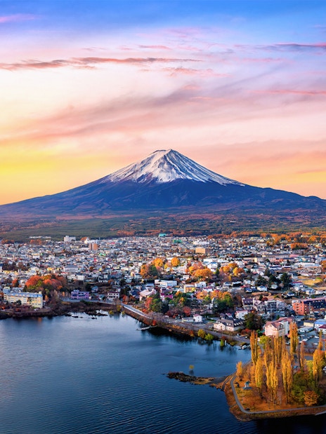 Aerial view of Mount Fuji with a cityscape and lake in the foreground at sunset.