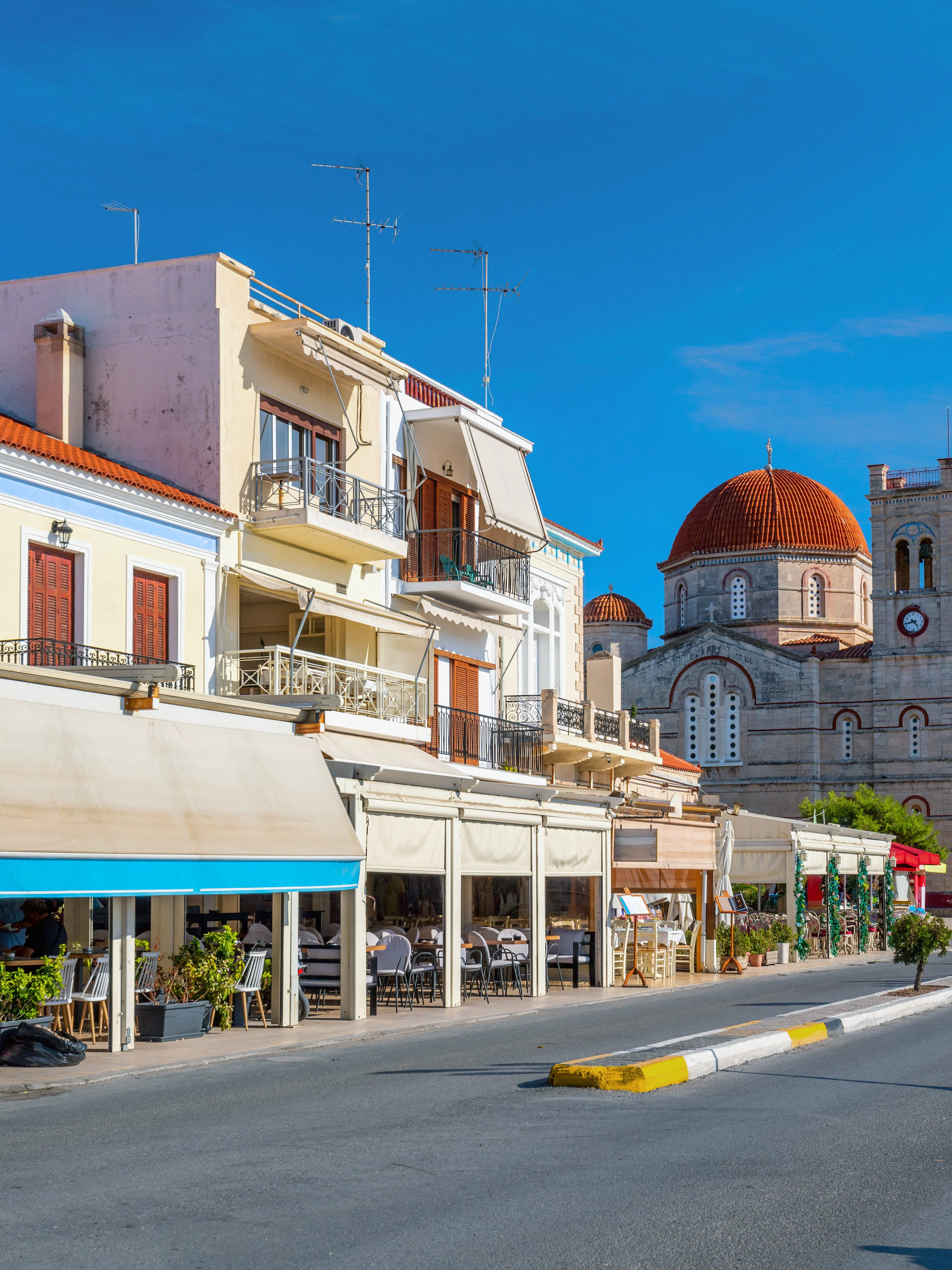 Street view of a small town on Aegina island with cafes and a church.