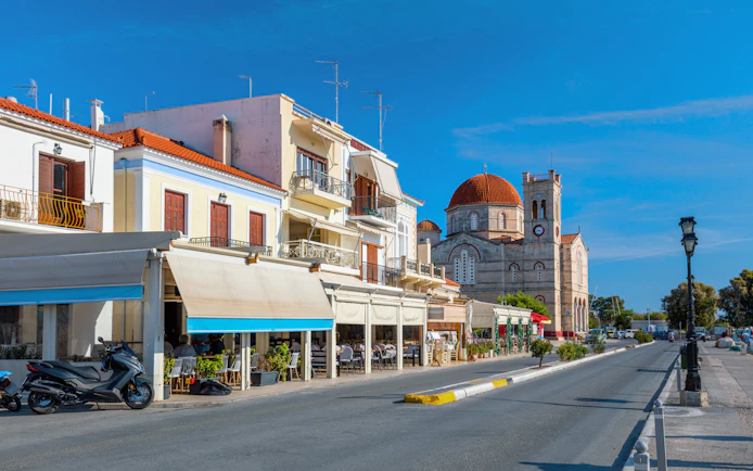 Street view of a small town on Aegina island with cafes and a church.