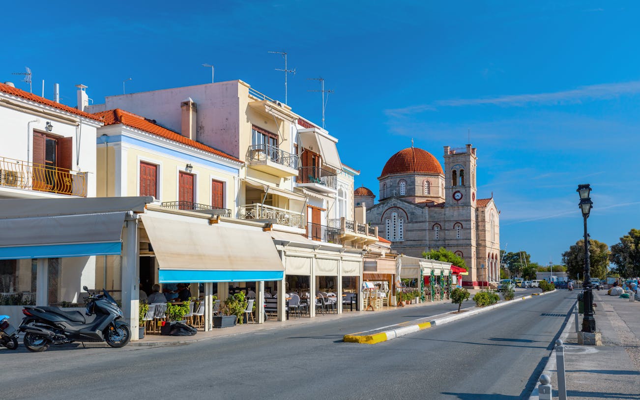 Street view of a small town on Aegina island with cafes and a church.