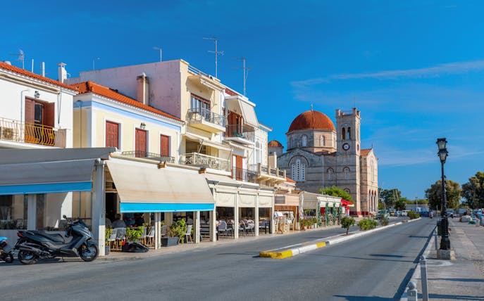 Street view of a small town on Aegina island with cafes and a church.