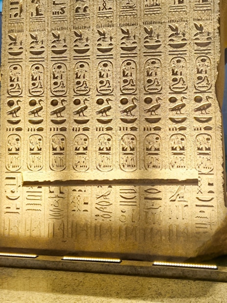 Hieroglyphs on stone slab at Grand Egyptian Museum, Cairo, with visitors exploring the exhibit.