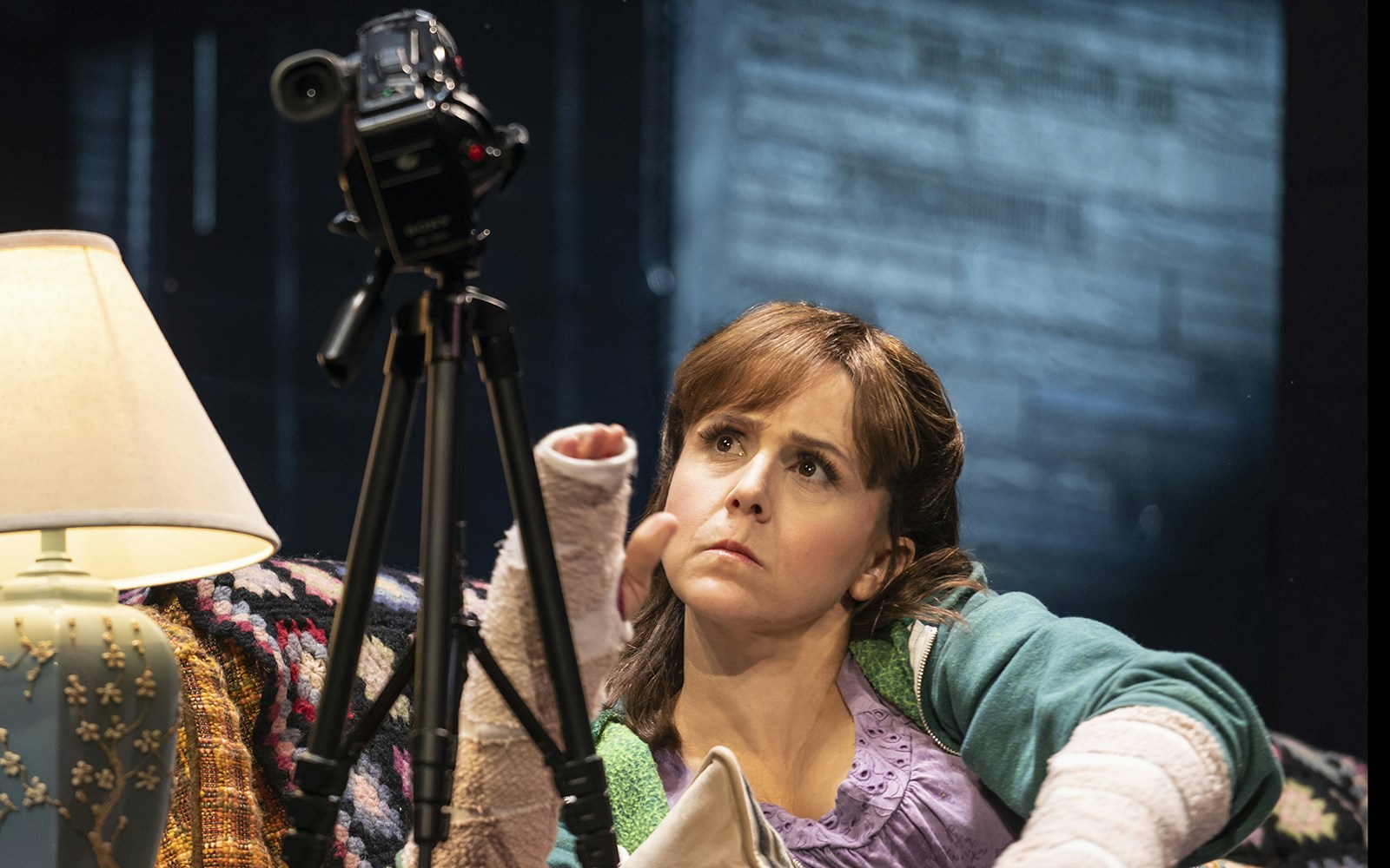 Woman with bandaged arms looking at a camera on a tripod at Booth Theatre.