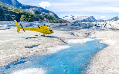 Yellow helicopter on a glacier with a blue stream in Juneau, Alaska.