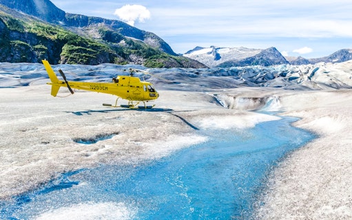 Yellow helicopter on a glacier with a blue stream in Juneau, Alaska.