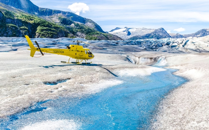 Yellow helicopter on a glacier with a blue stream in Juneau, Alaska.