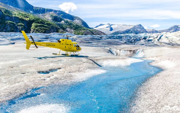 Yellow helicopter on a glacier with a blue stream in Juneau, Alaska.