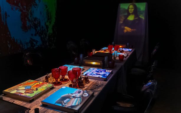 Immersive dining table set with art-themed decor and red glassware for Seven Paintings show.