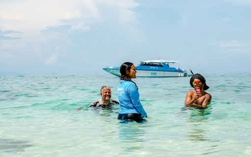 Guests and a tour guide swim in Phi Phi Island's turquoise water, with a speedboat in the background.