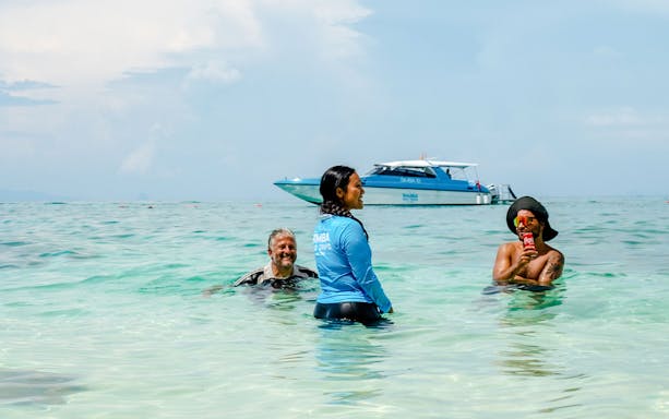 Guests and a tour guide swim in Phi Phi Island's turquoise water, with a speedboat in the background.