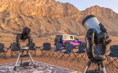 Telescopes and chairs set up for stargazing in Mleiha desert with mountains in the background.