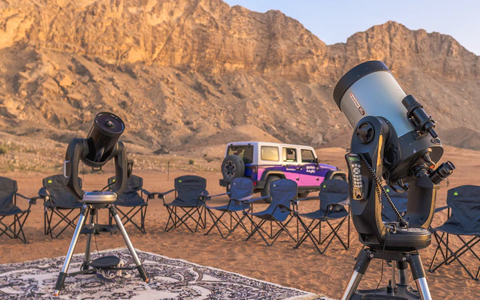 Telescopes and chairs set up for stargazing in Mleiha desert with mountains in the background.