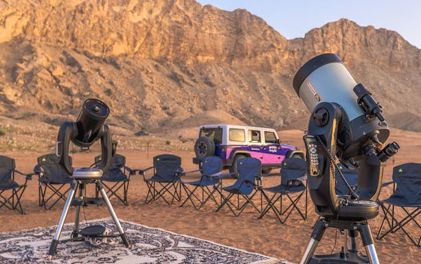 Telescopes and chairs set up for stargazing in Mleiha desert with mountains in the background.