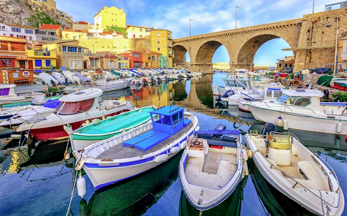 Boats docked in Vallon des Auffes bay, Marseille with stone bridge and colorful houses.