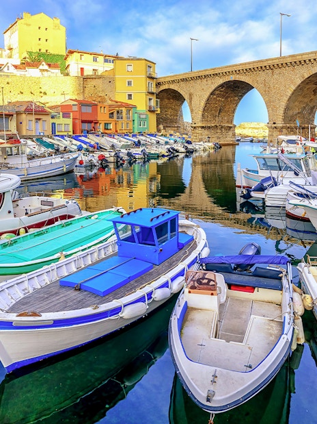 Boats docked in Vallon des Auffes bay, Marseille with stone bridge and colorful houses.