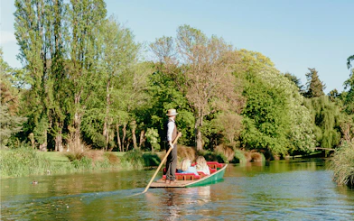 Punting on the Avon River in Christchurch with lush green trees in the background.