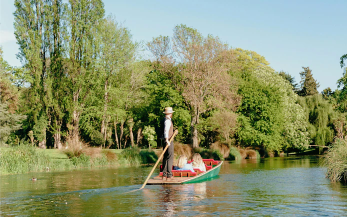 Punting on the Avon River in Christchurch with lush green trees in the background.