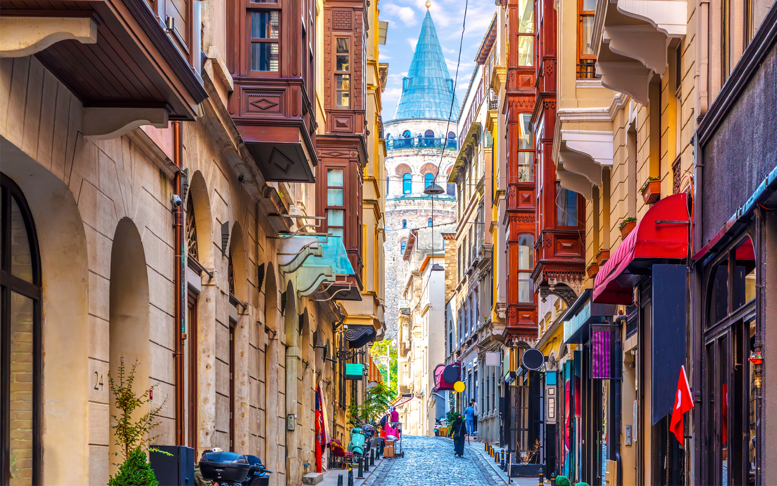 Galata Tower viewed from a narrow street in Istanbul, surrounded by historic buildings.
