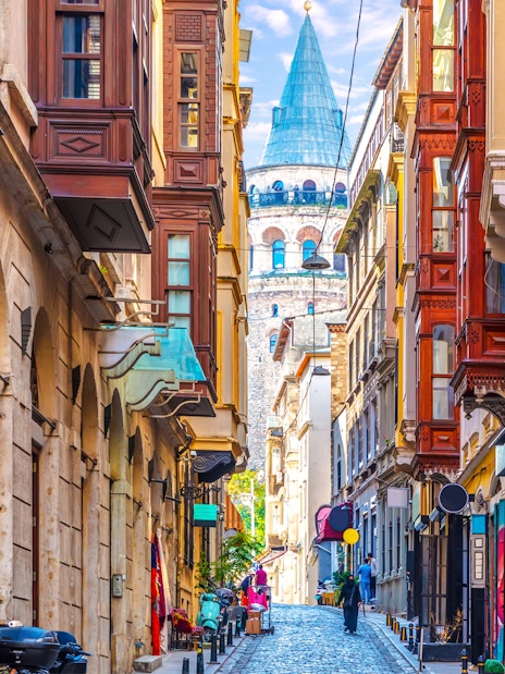 Galata Tower viewed from a narrow street in Istanbul, surrounded by historic buildings.