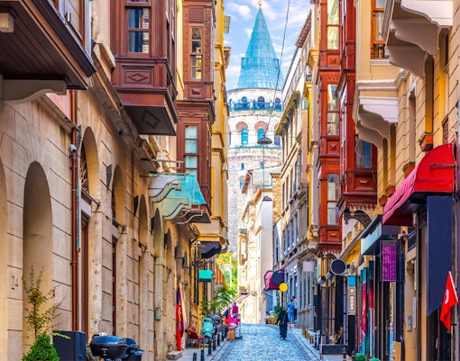 Galata Tower viewed from a narrow street in Istanbul, surrounded by historic buildings.