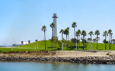 Lighthouse and palm trees at Los Angeles Harbor with Queen Mary ship in the background.