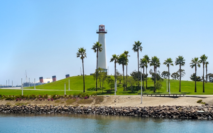 Lighthouse and palm trees at Los Angeles Harbor with Queen Mary ship in the background.