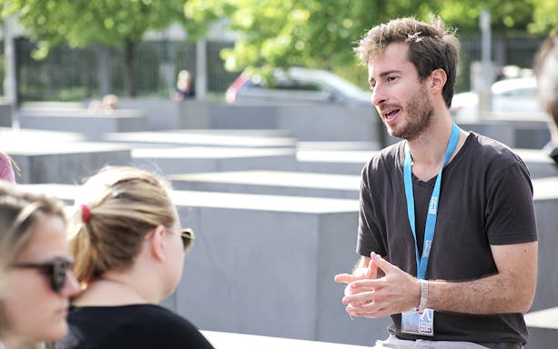 Tour guide explaining to tourists at an outdoor memorial site.