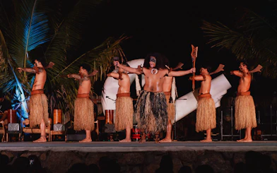 Mauka Warriors performing traditional dance at Hawaiian luau with palm trees in background.