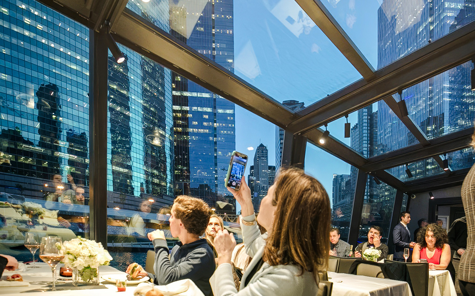 Guests dining on a Chicago dinner cruise with city skyline views through glass windows.