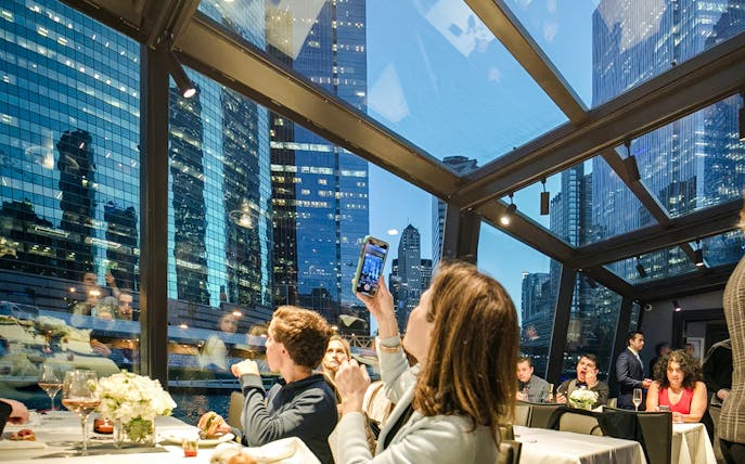 Guests dining on a Chicago dinner cruise with city skyline views through glass windows.